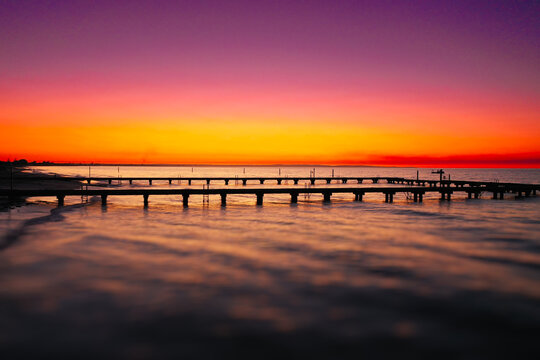 Aerial view of Busselton Jetty stretching into the calm ocean waters during a vibrant sunset with a colorful orange and purple sky in Busselton, Western Australia, Australia.