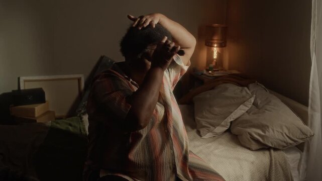 Medium shot of senior African American woman sitting on bed, combing her hair with pick comb. Clip is perfect for senior care services, mental health awareness, and daily routine commercial campaigns