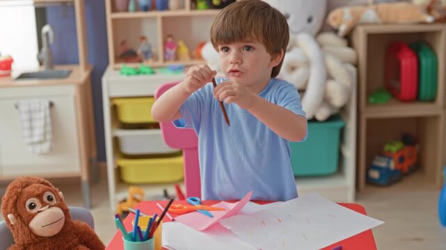 Boy drawing with crayon, hand reaching over paper at table inside building; childhood creativity concentration.