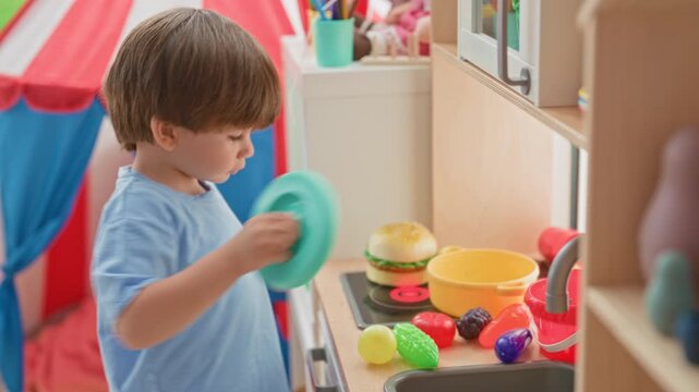 Little hispanic boy playing with toy kitchen, arranging plastic fruit and pan, reaches hand into sink in building; playful curiosity.