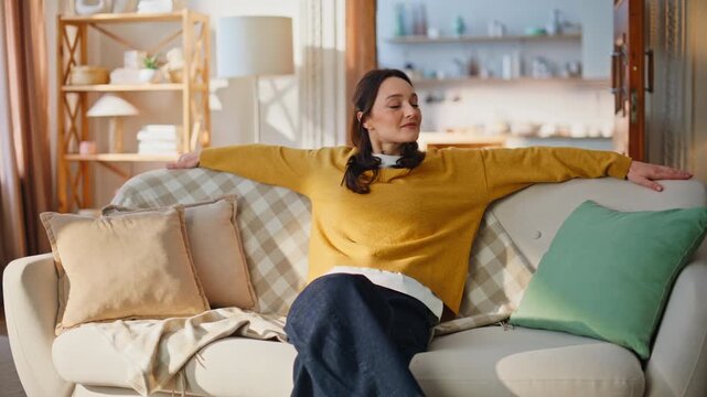 Woman leaning sofa back relaxing apartment after activities. Smiling brunette 