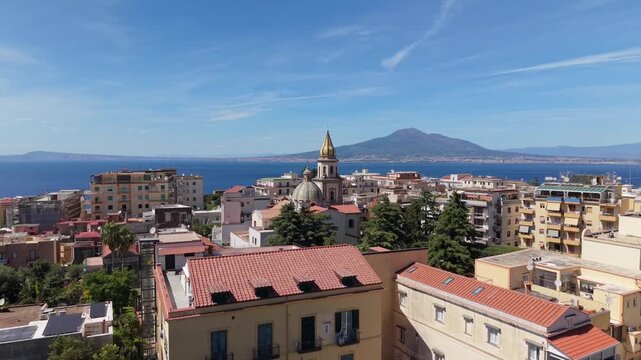 Aerial view of Vico Equense rooftops with Chiesa dei Santi Ciro e Giovanni golden bell tower and Mount Vesuvius volcano across Gulf of Naples, Italy
