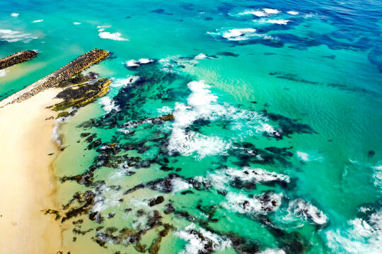 Aerial view of Kingscliff Beach with turquoise water, rocky outcrops, and a stone breakwater extending into the ocean in Kingscliff, New South Wales, Australia.