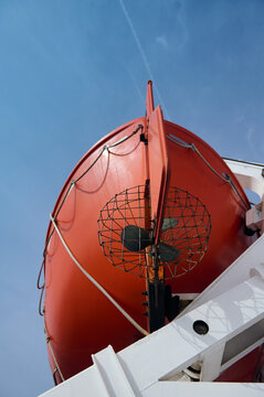 Orange lifeboat and davit on ship deck under clear blue sky, maritime safety and rescue equipment
