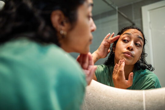 Young woman checking skin in bathroom mirror