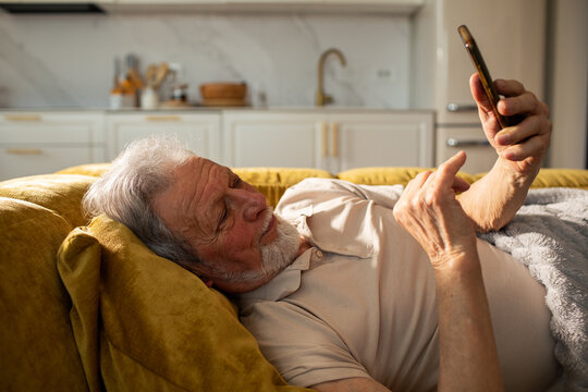 Senior man lying on couch using smartphone at home