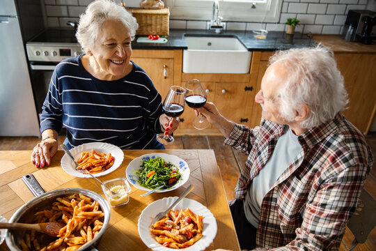 Senior couple toasting wine over pasta dinner at home kitchen