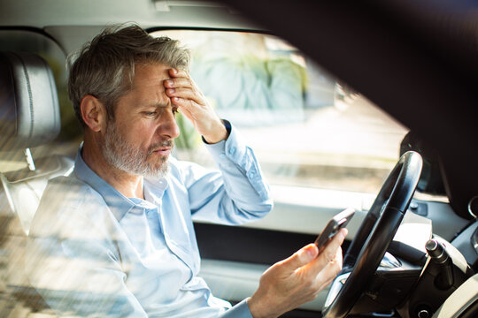Worried middle-aged man checking phone in car