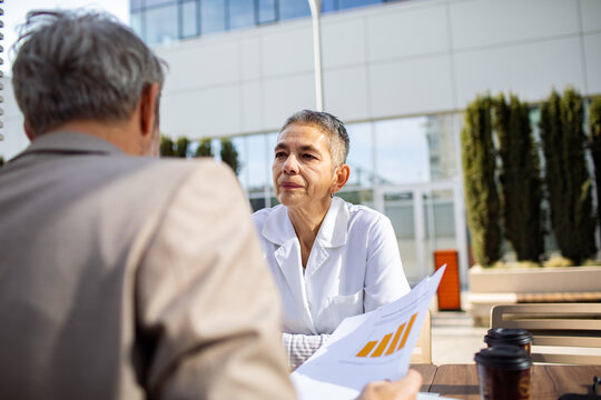 Two professionals discussing financial report outdoors at office