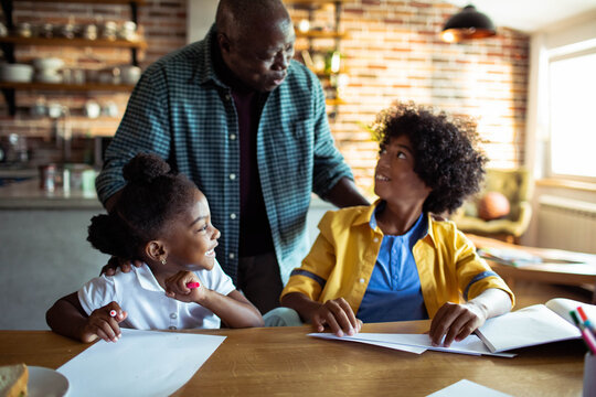 Grandfather helping children with homework at kitchen table