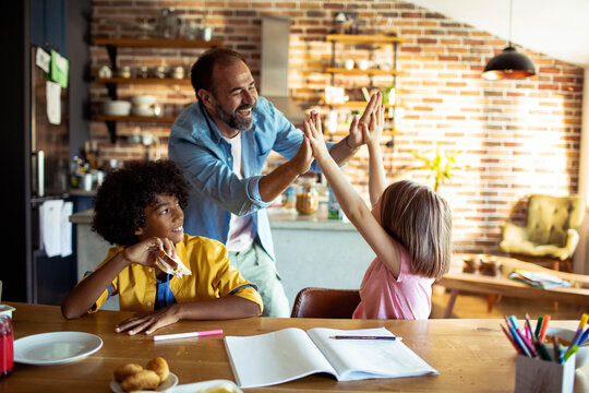 Father high fives daughter while helping kids with homework in kitchen