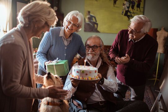 Senior friends celebrating birthday with cake and gifts at home
