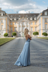 Obraz premium Woman stands on pathway in front of historic building wearing blue dress with arms crossed on a clear day