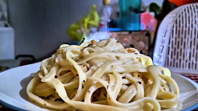 Close-up of steam rising from a freshly cooked hot plate of creamy fettuccine carbonara pasta with black pepper in a domestic setting.