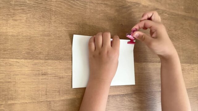 Child Hands Remove One of Two Pink Paper Clips from a Stack of Papers, 4K