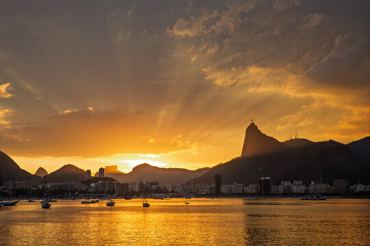 P&ocirc;r do sol com raios crepusculares sobre a Ba&iacute;a de Guanabara e silhueta do Corcovado, Rio de Janeiro, Brasil