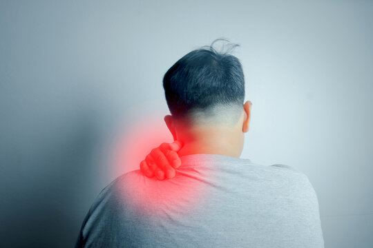 Rear view of man massaging his aching neck and shoulder with red highlight showing pain area. Office syndrome, muscle inflammation, and physical therapy healthcare treatment concept.