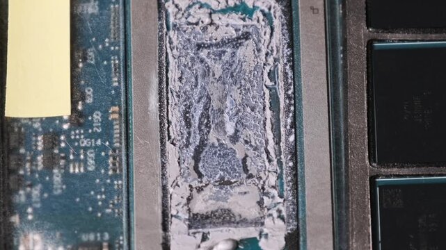 Old dried thermal paste covers the silicon die of a laptop processor on a circuit board. Concept of hardware maintenance, overheating prevention, and technical computer repair.