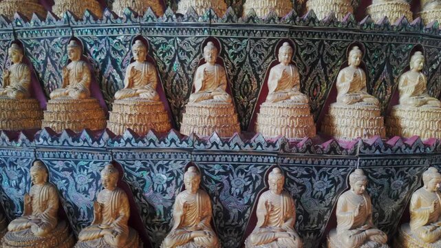 Rows of golden Buddha statues adorn a temple wall in Wat Sam Phran, Nakhon Pathom, Thailand. The intricate mother-of-pearl inlay depicts mythical birds and floral motifs.