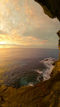 Fisheye video of sunrise over the ocean along the Sydney coastline, with calm water and rugged coastal cliffs glowing in soft golden morning light, Australia.
