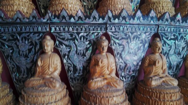 Rows of golden Buddha statues adorn a temple wall in Wat Sam Phran, Nakhon Pathom, Thailand. The intricate mother-of-pearl inlay depicts mythical birds and floral motifs.