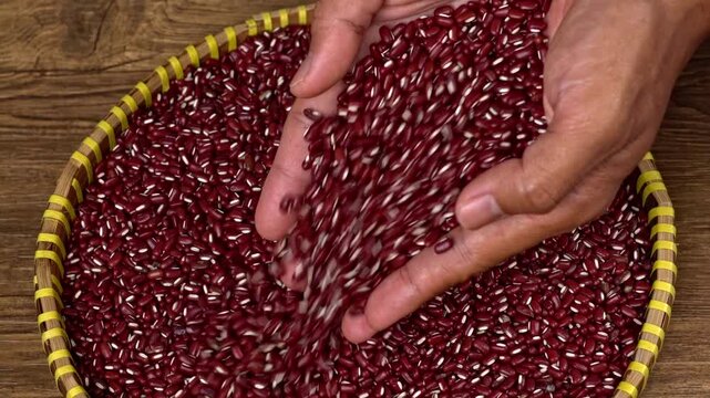 Close up view of hands pouring vibrant red beans into a rustic woven basket on a wooden surface
