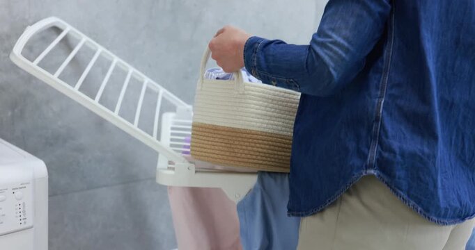 Woman putting different clothes onto drying rack indoors, closeup. Camera moving up