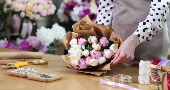 Florist wrapping bouquet of beautiful peonies in paper at table indoors, closeup