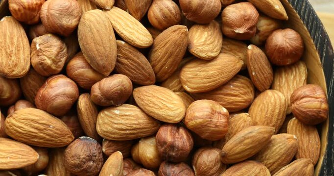 Vegan snack. Tasty hazelnuts and almonds spinning in bowl, top view