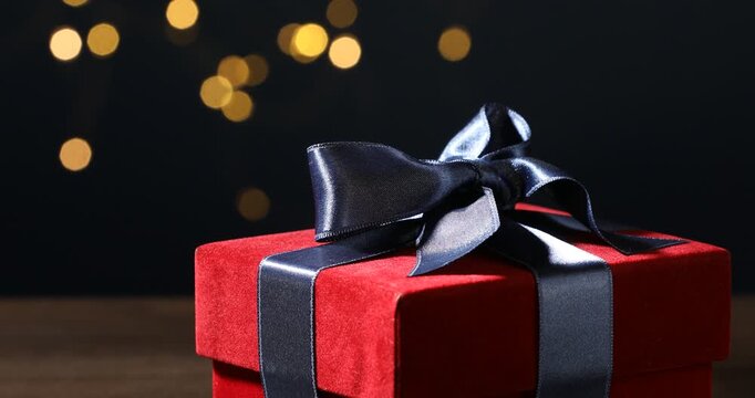Woman putting beautiful velvet gift boxes onto table against black background with blurred lights, closeup. Bokeh effect