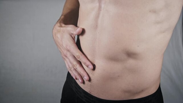 Side view close-up of a lean man rubbing his toned stomach and obliques. The athletic build highlights physical fitness while checking for muscle strain or cramps.