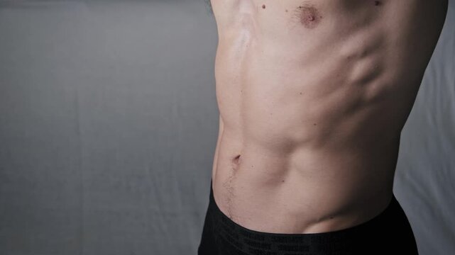 Close-up of an athletic man performing a stomach vacuum pose to demonstrate core control. He inhales deeply to pull in his abdomen and highlight defined rib cage muscles.