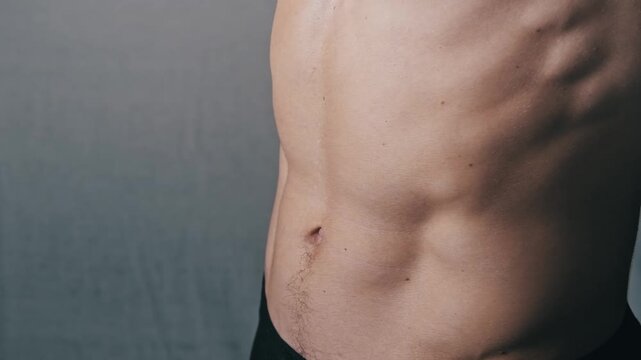 Frontal close-up view of a mans muscular torso. He places his hands on his stomach to frame and showcase his well-defined six-pack abs highlighting physical fitness.