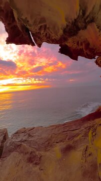 Slow motion fisheye video of sunrise over the ocean framed by a natural rock opening along the Sydney coastline, with calm water reflecting soft golden morning light, Australia.