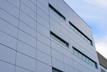 Fototapeta premium The exterior wall of a contemporary commercial style building with aluminum metal composite panels and glass windows. The futuristic building has engineered diagonal cladding steel frame panels.