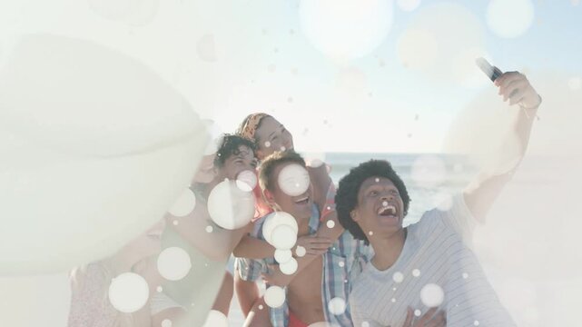 Six friends huddling beach as bokeh overlay fading revealing right raising phone for social selfie