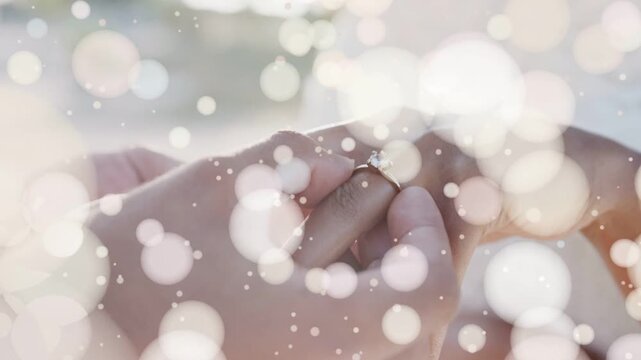 Camera focusing through bokeh, man placing diamond ring onto woman's finger, completing wedding