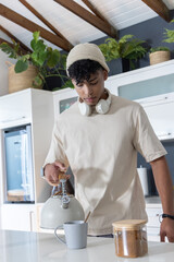 African American man in beanie and headset pouring water from kettle into mug at kitchen counter © wavebreak3