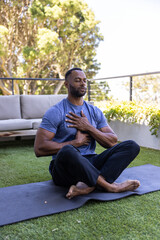 Obraz premium African American man sitting cross-legged meditating on mat rooftop in blue shirt and black pants