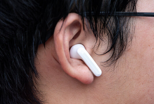 Close-up of a person wearing a white wireless earbud in ear.  A macro close-up shot capturing a modern white wireless earbud securely fitted into a person's ear. 