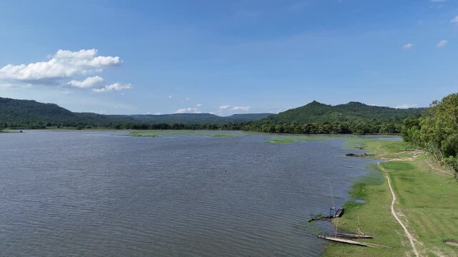 Scenic landscape of Huai Phueng reservoir with a lush green mountain range under a clear blue sky in Kalasin, Thailand.