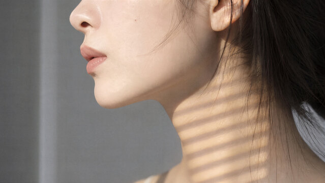 Gentle Portrait: A close-up profile shot focuses on the delicate features of a young woman's face and neck, illuminated by soft, striped sunlight filtering through blinds.