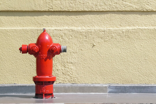 Bright red fire hydrant on concrete sidewalk against textured yellow wall, safety equipment, emergency urban utility