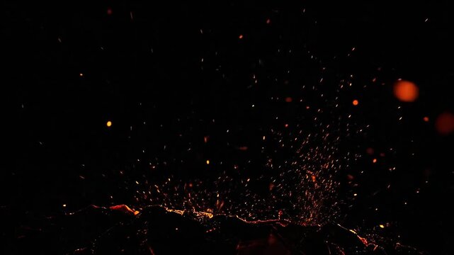 Glowing fire sparks rising from burning embers against a black background