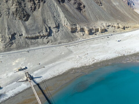 Aerial view of the Keris valley featuring a turquoise river, a suspension bridge, and rugged mountain slopes in Yugo, Gilgit Baltistan, Pakistan.