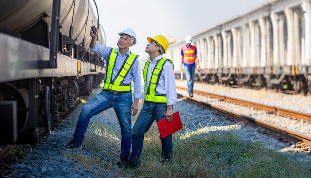 Engineers team inspecting freight tank cars at railway depot, Railway transport inspection with experts at freight train terminal, Workers inspecting train undercarriage during maintenance check