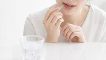 Fototapeta premium Oral Hygiene Ritual: A young woman meticulously cleans her teeth with a toothpick, beside a glass of water, focusing on a moment of personal care and well-being.