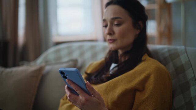 Serious brunette receiving message cellphone sitting sofa closeup. Upset woman