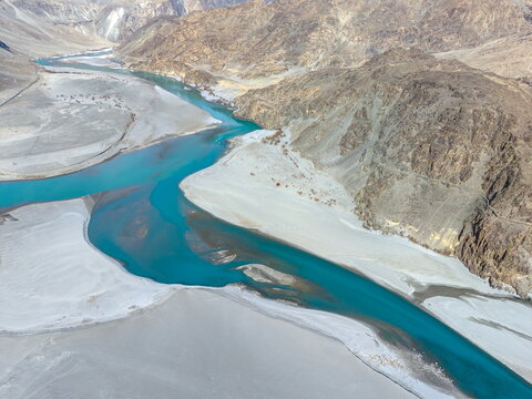 Aerial view of the turquoise river winding through the rugged landscape of the Keris valley with sandy riverbanks and towering mountain slopes in Yugo, Gilgit Baltistan, Pakistan.