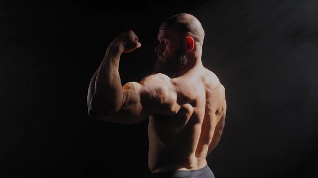 A male bodybuilder poses in shorts, showing off his back muscles.